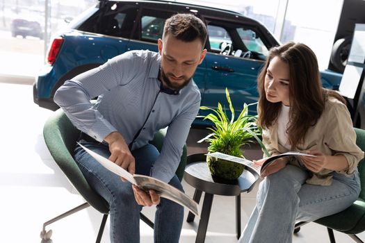 a married couple sitting in a car dealership chooses a new car from the catalog.