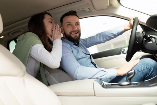 a young married couple in a car dealership chooses a new car whispering among themselves.