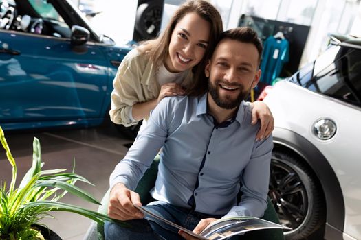 happy young couple with smiles on their faces at car dealership showroom getting ready to buy a new car.