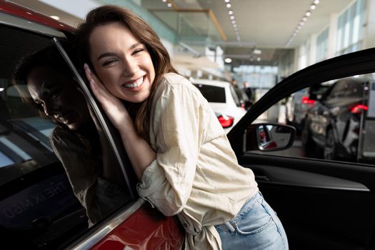 young woman rejoices in buying a new car in a car dealership.