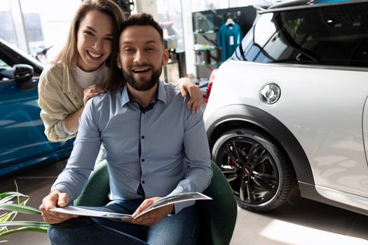 a young married couple studying a booklet before buying a new car, the concept of personal transport insurance.