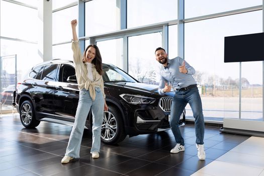 satisfied young couple dancing next to a new purchased car from a car dealership.