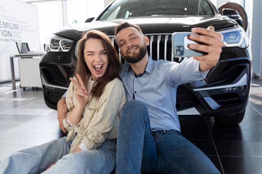 a young happy family couple is photographed next to a new purchased SUV in a car dealership.