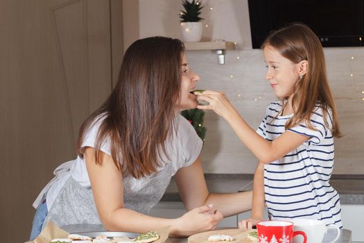 A little girl feeds her mother with cooked cookies in the kitchen. Real life. The concept of cooking with children.