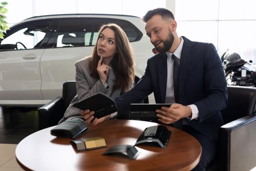 a young married couple in a car dealership chooses a car sits with a smile in the trunk of a crossover.