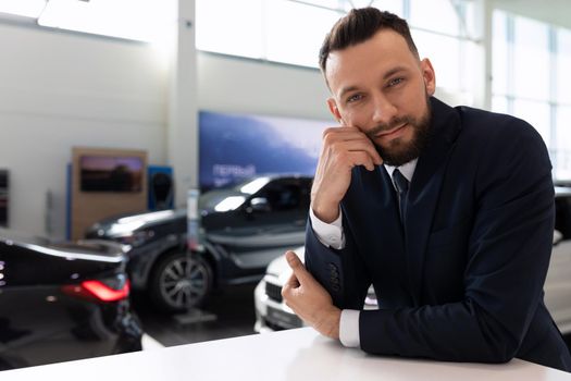 portrait of an employee of a car dealership in the showroom against the background of new cars.