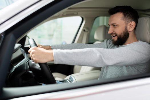 novice driver behind the wheel of a new car looks ahead with a smile.