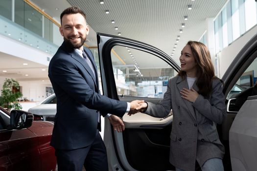 an employee of a car dealership helps a young woman with a choice of a new car.