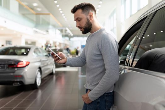 a man on the phone studies the features of an SUV in a car dealership.