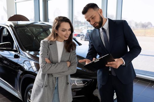 an employee of a car shop draws up documents for a new car for a woman buyer.