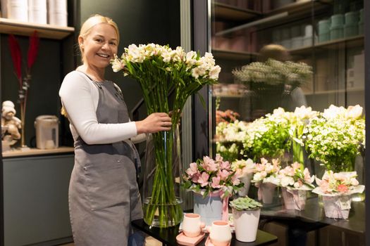 flower shop employee next to a refrigerator with fresh flowers for bouquets.