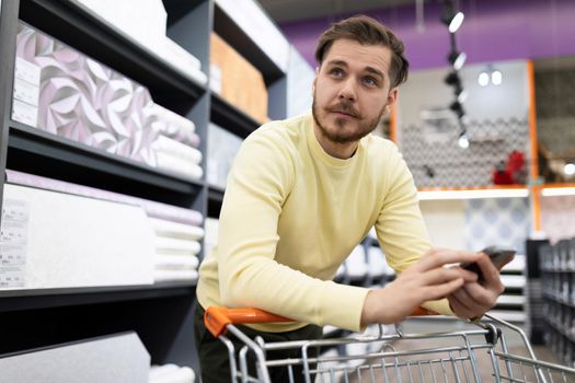 a man in a hardware store chooses decorative wallpaper for the walls.