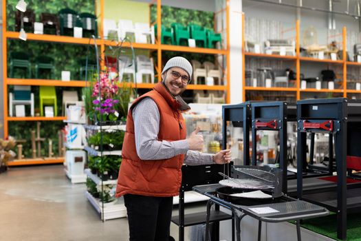 a customer in a picnic supply store picks up a grill and barbecue for outdoor recreation.