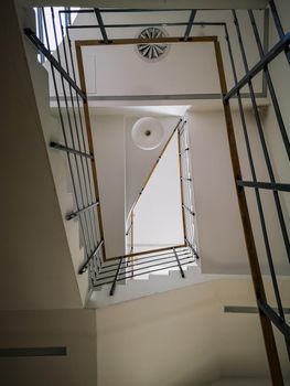 Looking up to Rectangular staircase with light wooden handrail and white ceiling