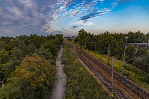 Beautiful cloudy sunset seen from long high concrete footbridge over city highway and train rails