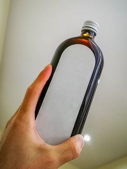 Wide high dark bottle with white label holded in hand