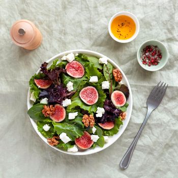 portion of fig, green salad leaves, feta cheese and walnuts salad, top view