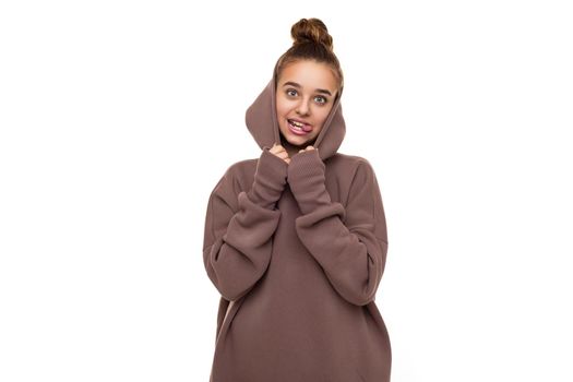 Photo of a beautiful funny cute girl with dark hair and a bun in a brown hoodie with a hood isolated on a white background and shows tongue.