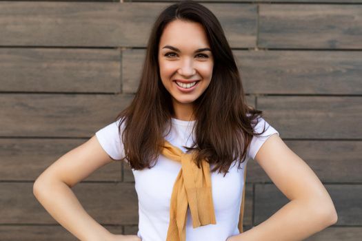 Close-up photo of pretty attractive beautiful smiling happy positive charming young brunette young woman wearing stylish clothes in the street near brown wall.