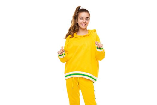 Beautiful funny happy wonderful smiling cute girl with dark hair with ponytail in stylish yellow tracksuit with green stripes isolated on white background with empty space for text.