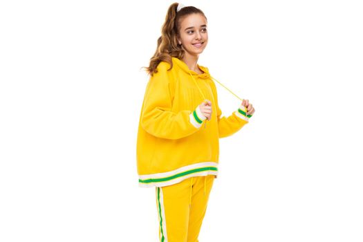 Photo of beautiful funny happy wonderful smiling cute girl with dark hair with ponytail in stylish yellow tracksuit with green stripes isolated on white background with free space for text.