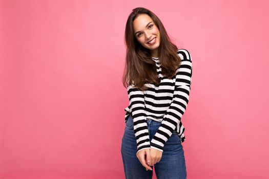 Photo of young european positive smiling winsome happy beautiful brunette woman with sincere emotions wearing casual striped pullover isolated on pink background with copy space for text.