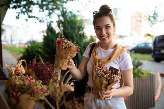 Young positive happy beautiful pretty brunette woman enjoying flowers in pots on the porch of a flower shop and smiling at the camera.