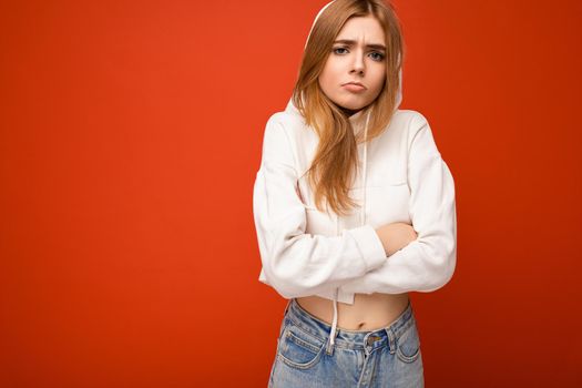 Dissatisfied angry young beautiful dark blonde female person with sincere emotions isolated on background wall with copy space for text wearing casual white hoodie. Negative concept.