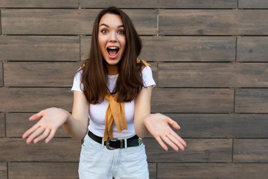 Close-up photo of pretty attractive beautiful happy positive charming amazed surprised shocked young brunette young woman wearing stylish clothes in the street near brown wall.