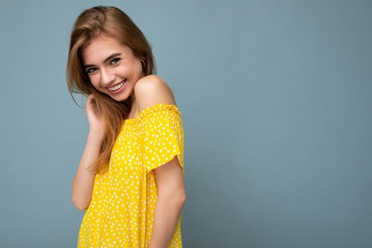 Photo of young cute delightful beautiful attractive dark blonde woman with sincere emotions isolated on blue background wall with copy space for text wearing stylish yellow dress. Positive concept.