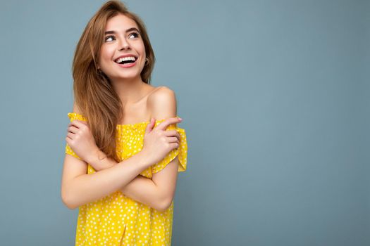 Photo of young cute delightful beautiful attractive smiling positive happy dark blonde woman with sincere emotions isolated on blue background wall with copy space for text wearing stylish yellow dress. Positive concept.