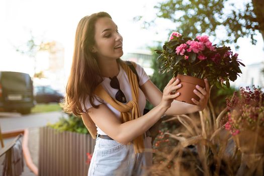 Photo of european beautiful attractive positive happy brunette woman wearing stylish white t-shirt and blue jeans chooses flowers as a gift in a street garden stall in the town.