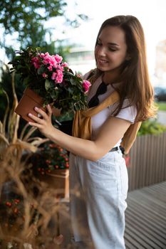 Vertical photo shot of european amazing beautiful attractive positive happy smiling young brunette woman in casual stylish look buys flowers in the store in the city.