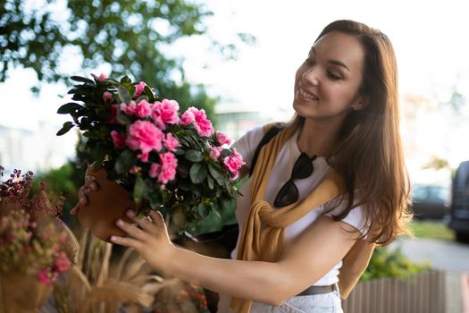 European beautiful attractive brunette female person wearing stylish white t-shirt and blue jeans chooses flowers as a gift in a street garden store in the town.