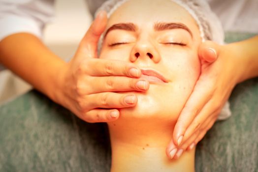 Beautiful young caucasian woman with closed eyes receiving a facial massage in a beauty salon