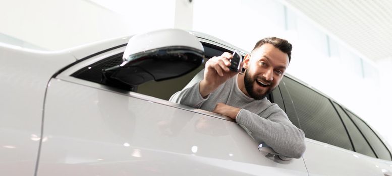 a man inside a new SUV in a car dealership showroom with a smile on his face.