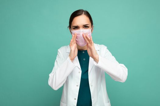 Shot of female person doctor in a white medical coat wearing protective mask isolated on green background with empty space for text and shouting. Epidemic concept.
