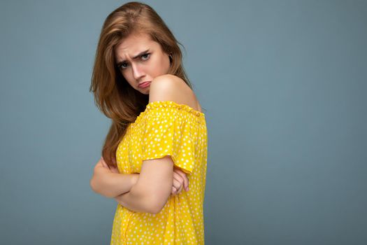 Photo of young cute delightful beautiful attractive sad dissatisfied unhappy dark blonde woman with sincere emotions isolated on blue background wall with copy space for text wearing stylish yellow dress.