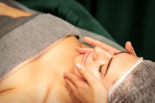 Beautiful young caucasian woman with closed eyes receiving a facial massage in a beauty salon