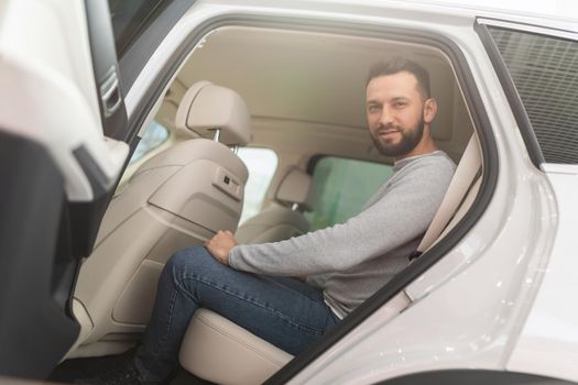 a man reconciles to a new car in a dealer showroom sitting in the back seat.