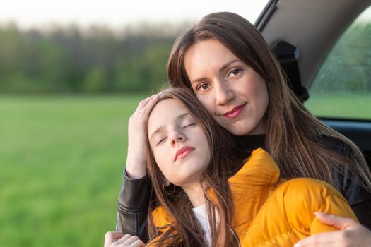 Mother and daughter camping on a hill and admiring the sunset while sitting in the car trunk