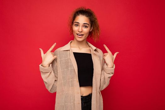 Photo of young positive happy attractive brunette wavy-haired woman with sincere emotions wearing casual beige shirt isolated on red background with empty space.