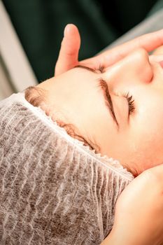 Face massage. Beautiful caucasian young white woman having a facial massage with closed eyes in a spa salon