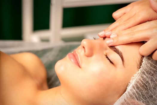 Head massage. Beautiful caucasian young white woman receiving a head and forehead massage with closed eyes in a spa salon