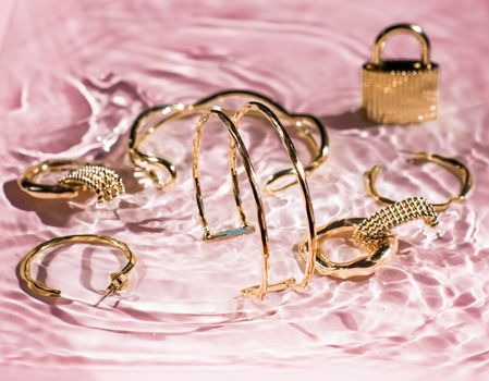 Jewellery branding, fashion gift and luxe shopping concept - Golden bracelets, earrings, rings, jewelery on pink water background, luxury glamour and holiday beauty design for jewelry brand ads