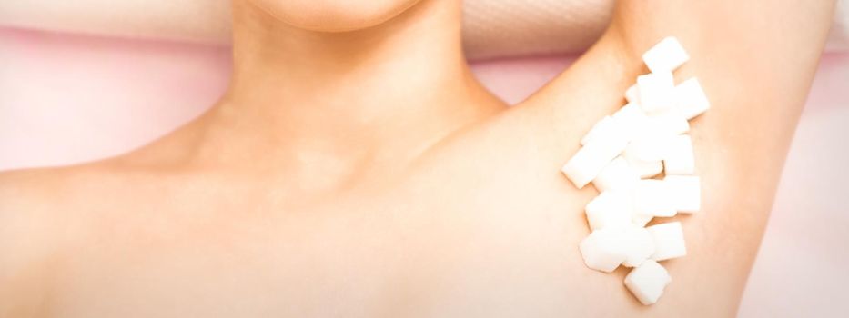 Sugaring, waxing concept. White sugar cubes lie down on the female armpit of the young white woman, close up