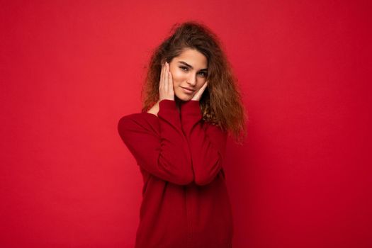 Young beautiful self-confident curly brunette woman with sincere emotions poising isolated on background wall with copy space wearing casual dark red sweater. Positive concept.