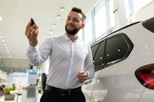 confident man with keys to a new car in a car dealership.