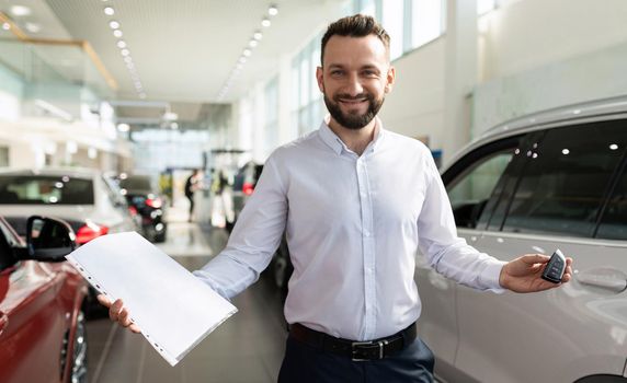 the owner of a new car in a dealer showroom demonstrates documents and keys from a new car.