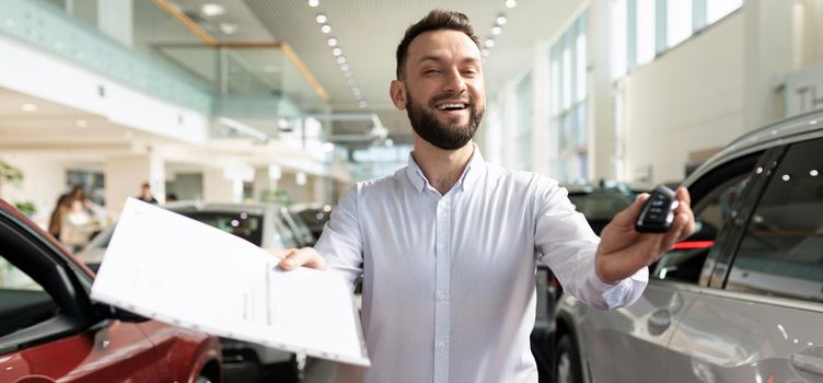 car dealership worker handing keys and documents from a new car to a happy buyer.